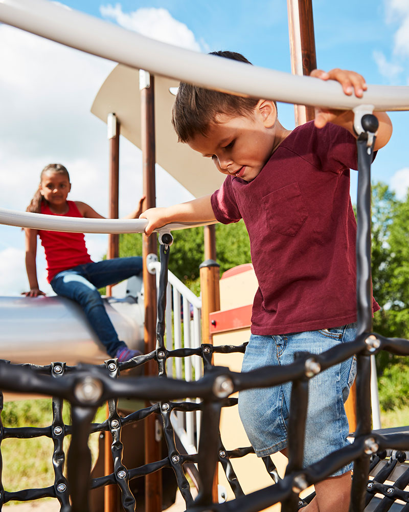 Ein kleiner Junge konzentriert sich, während er über eine Netzbrücke auf einem Spielplatz läuft.